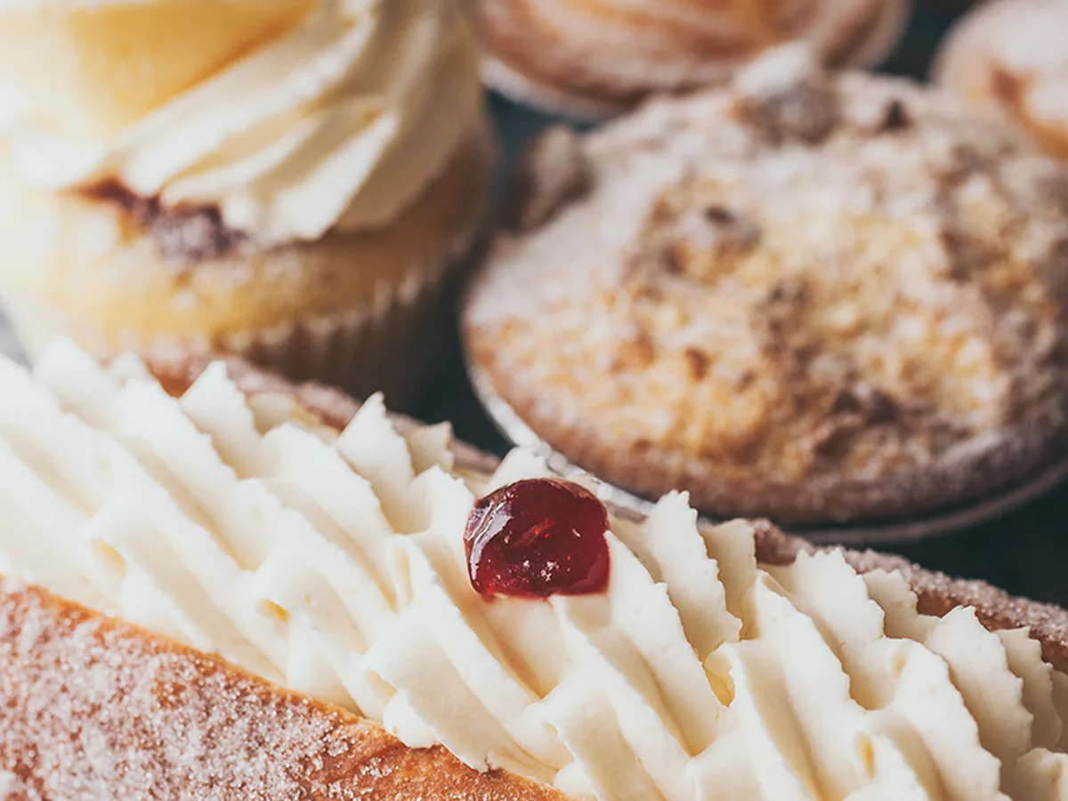 A cream filled finger bun with cupcakes behind it.