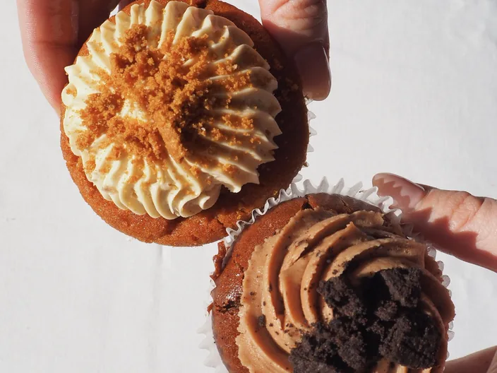 Two iced cupcakes held up, one caramel and one chocolate.